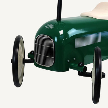 A close-up of the front of a green ride-on toy car showing a chrome grille, front axle, wheel and the lower edge of the body.