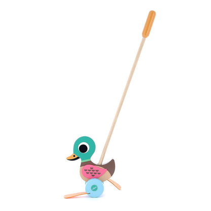 A side view of a wooden duck push toy with a long stick handle and orange grip, showing the toy’s green head, pink wings, and blue wheels.