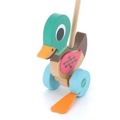 A close-up of a wooden duck push toy showing the details of its green head, orange beak, pink body markings, and sturdy blue wheels.