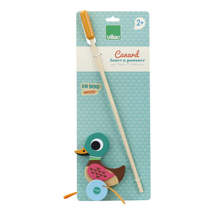 A packaged wooden duck push toy displayed on a blue backing card, with the stick handle attached and labelled for children aged 2 years and older.