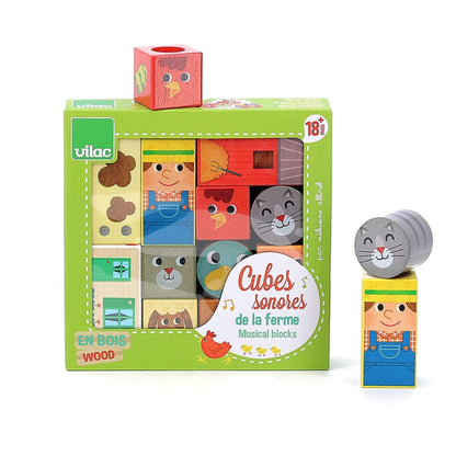 Wooden Musical Blocks boxed set in green packaging, with cubes featuring animals, farmer, and buildings, plus loose blocks of a cat and farmer.