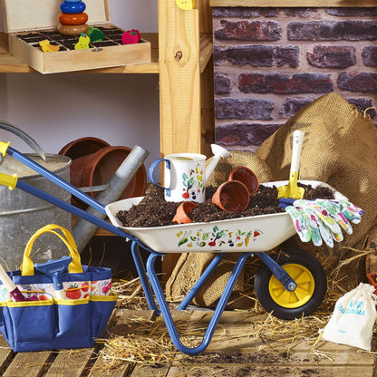 A children’s toy wheelbarrow filled with soil, plant pots and gardening tools in a shed setting, showing realistic outdoor play use.