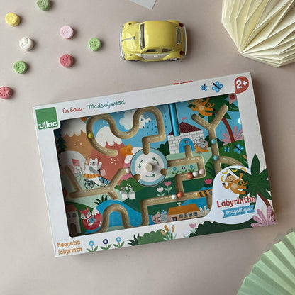 Boxed Vilac magnetic maze placed on a table with a toy car and pastel sweets around it, highlighting the packaging and product inside.