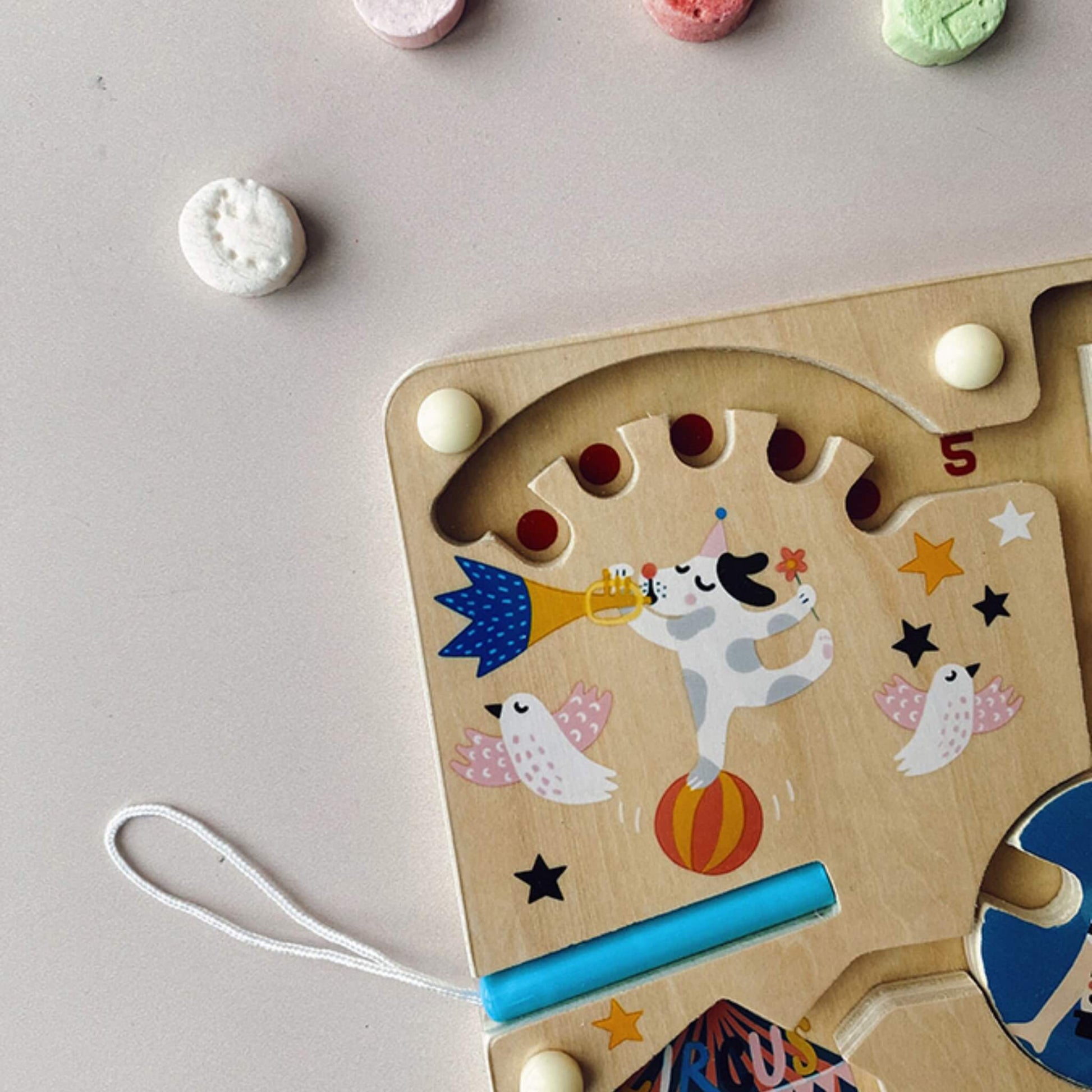 Close-up of the top left corner of the circus magnetic maze, showing a performing dog blowing a trumpet while balancing on a ball, with doves flying around.