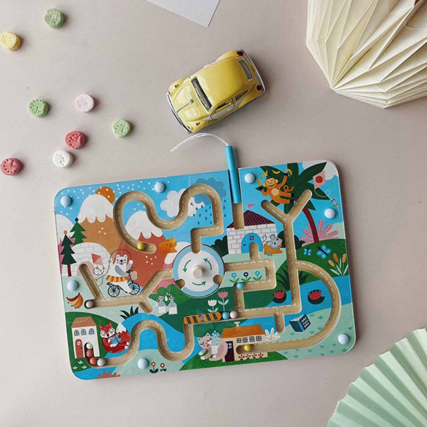 A magnetic maze board placed on a table with a toy car beside it and small sweets scattered around, showing the play scene in use.