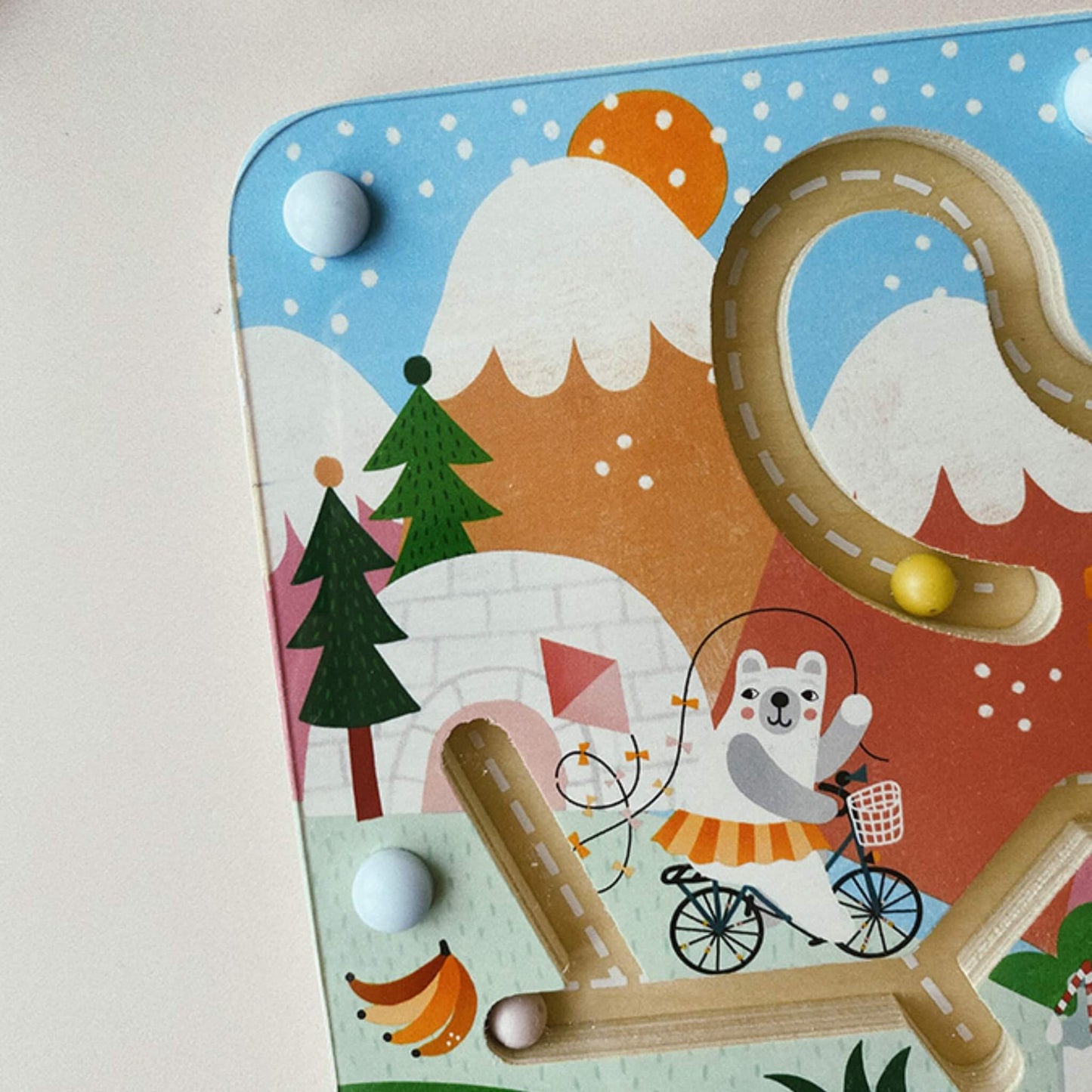 Close-up of the top left section of the magnetic maze, showing a bear illustration riding a bicycle, trees, mountains and a yellow magnetic bead on the track.