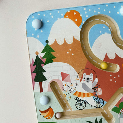 Close-up of the top left section of the magnetic maze, showing a bear illustration riding a bicycle, trees, mountains and a yellow magnetic bead on the track.