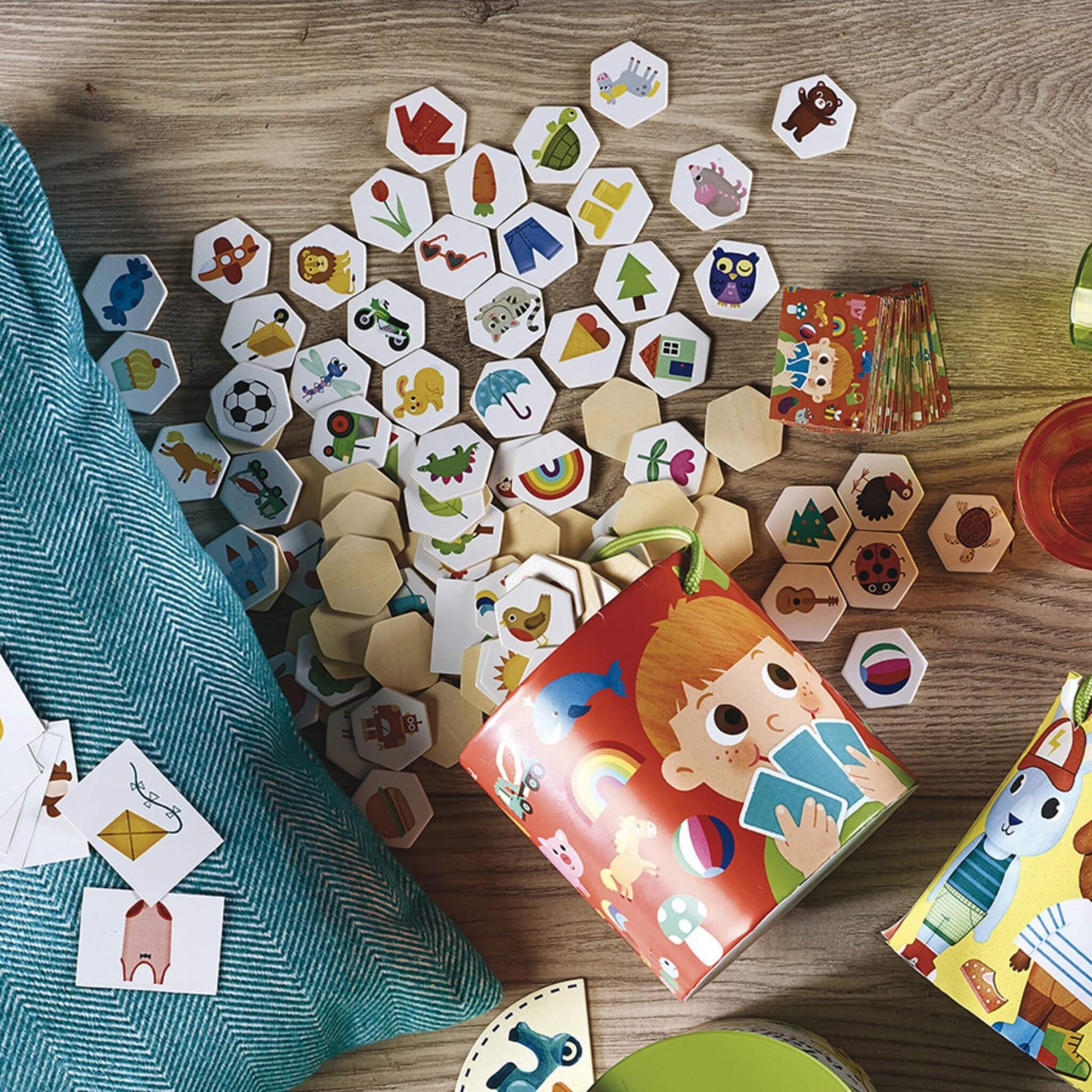 A set of illustrated hexagonal wooden tiles and matching picture cards arranged on a table during play, with a child’s game box beside them.
