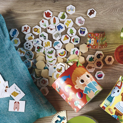 A set of illustrated hexagonal wooden tiles and matching picture cards arranged on a table during play, with a child’s game box beside them.