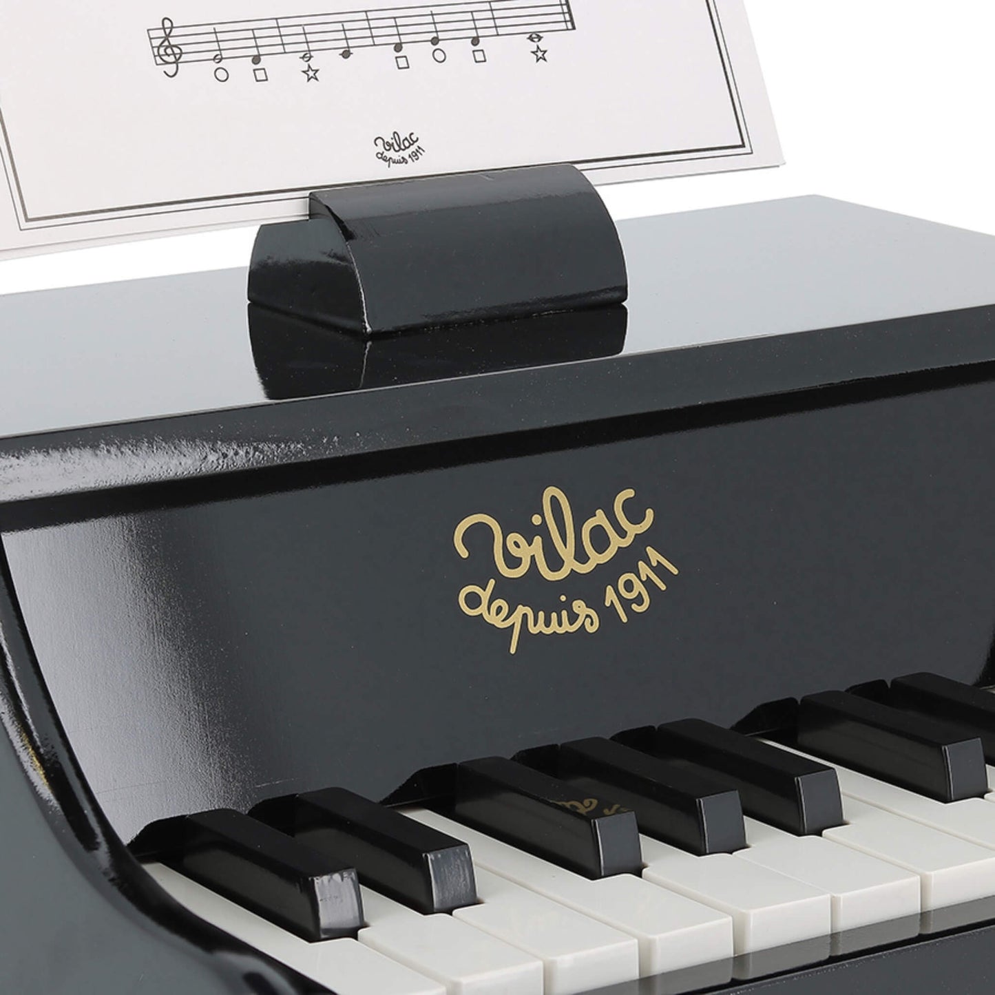 Close-up of the black toy piano keyboard showing white and black keys, with the gold Vilac logo above and a music sheet in the holder.