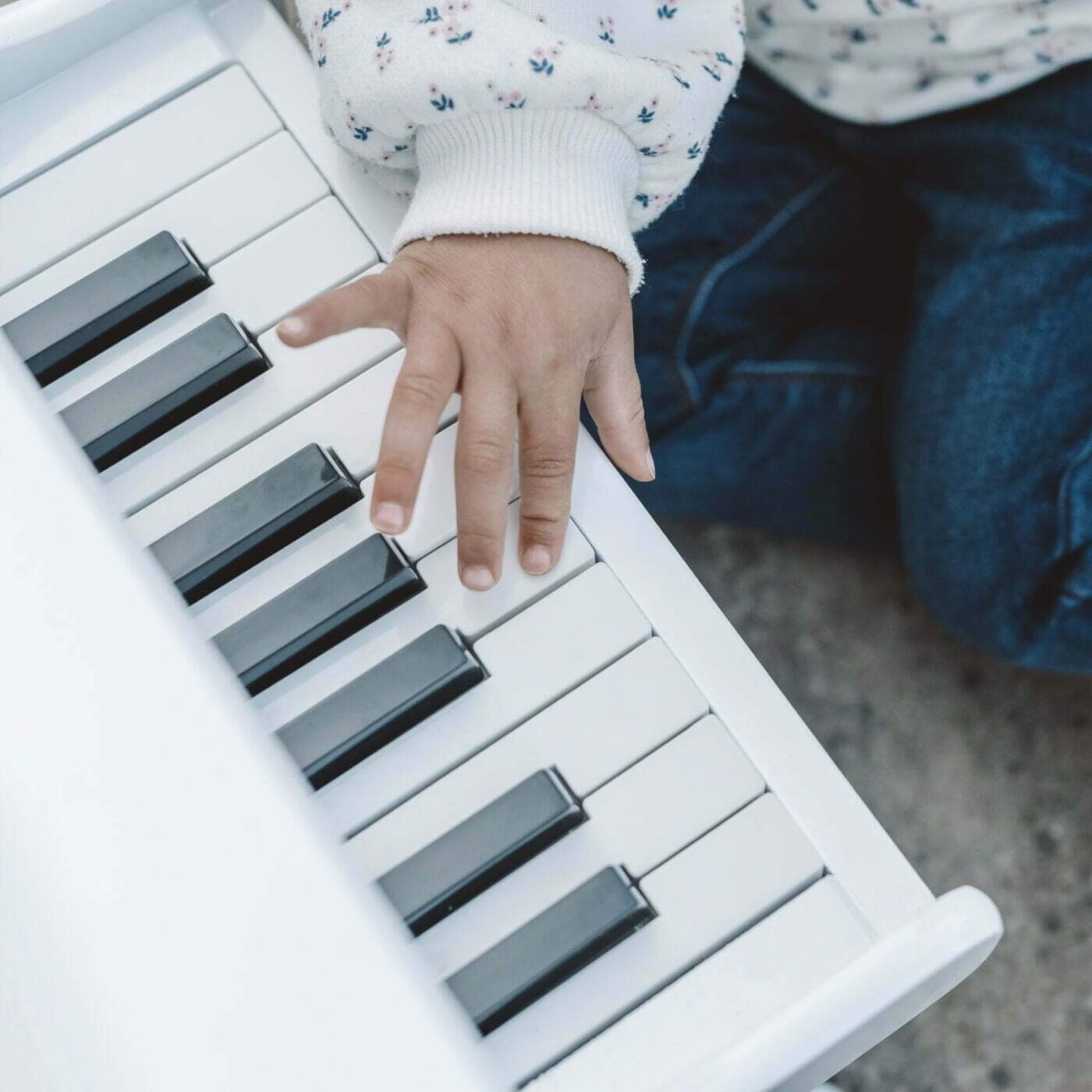 Close-up of a child’s hand pressing the keys of a white wooden toy piano, showing detail of the keyboard.