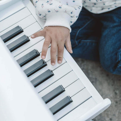 Close-up of a child’s hand pressing the keys of a white wooden toy piano, showing detail of the keyboard.