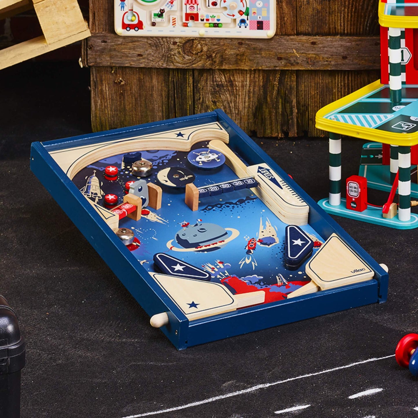 Wooden pinball game set up on the floor in a playroom, styled with other children’s toys around.