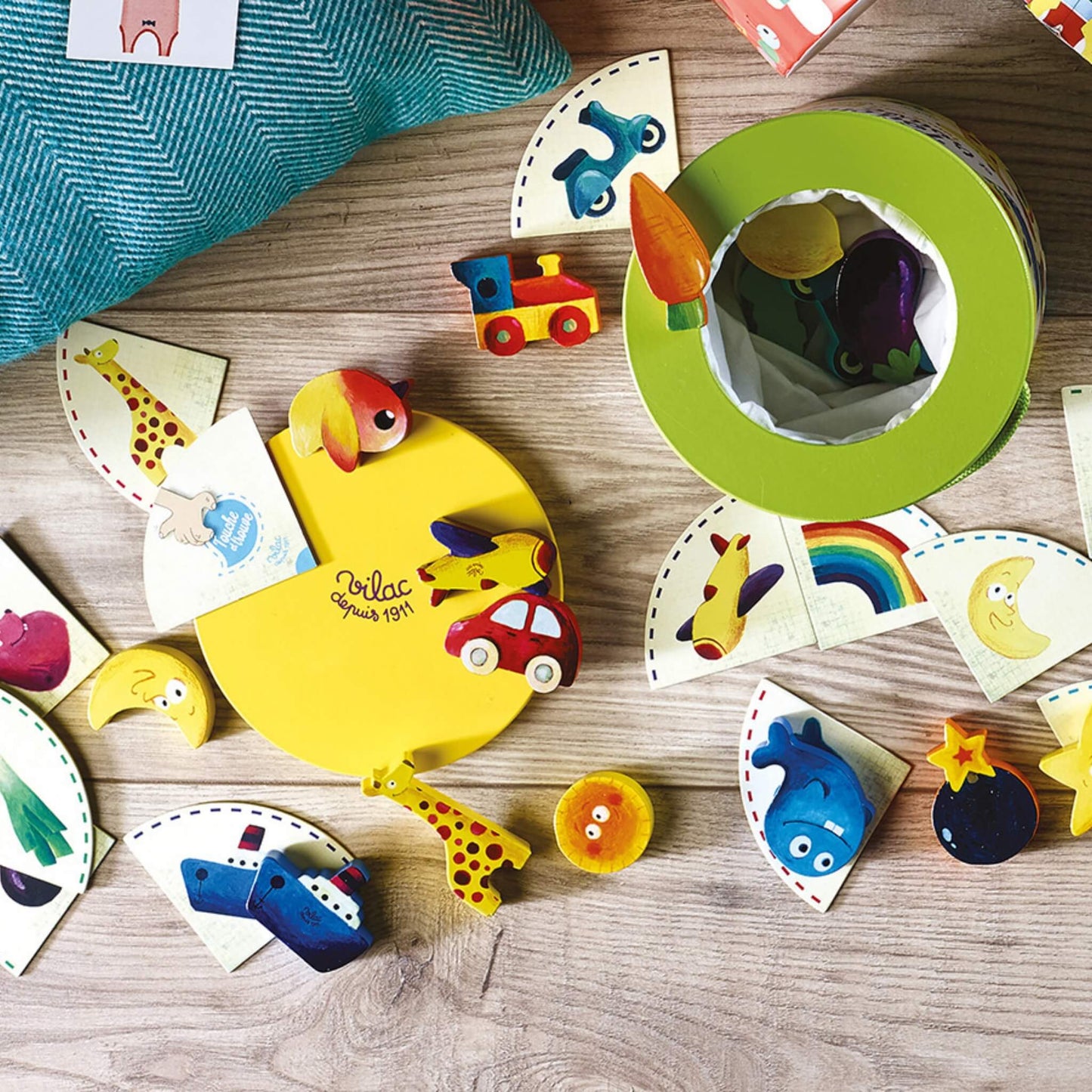 Wooden toy pieces including animals, vehicles and food items laid out with matching picture cards around an open barrel.