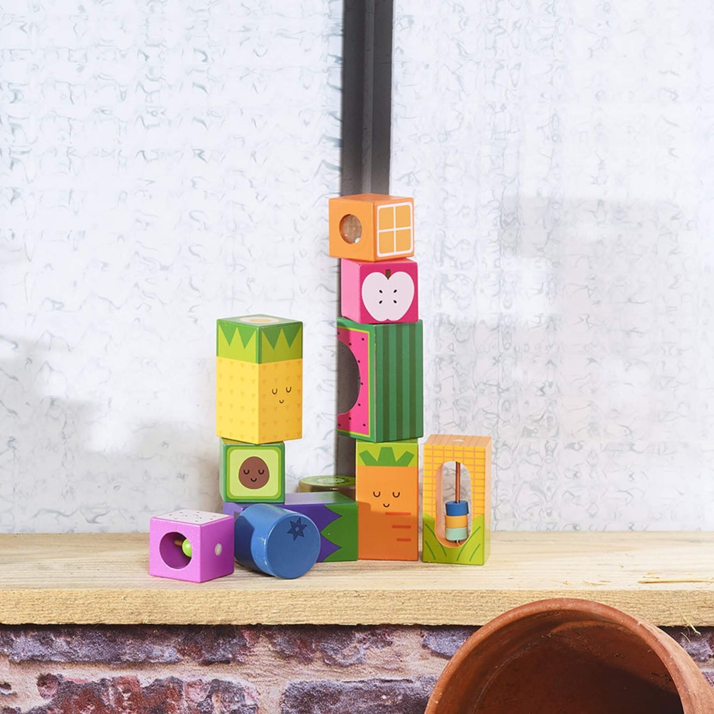 Wooden fruit and vegetable blocks stacked into a tall tower on a wooden surface, with additional blocks scattered nearby.