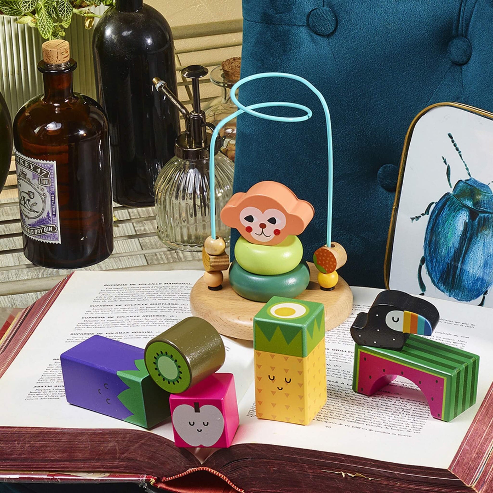 Wooden fruit and vegetable blocks placed on an open book next to a wooden bead maze toy shaped like a monkey.