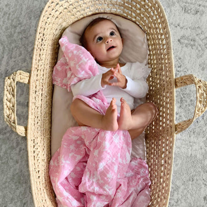 Baby lying in a woven basket with an Aden + Anais muslin swaddle in Ma Fleur pink floral print.