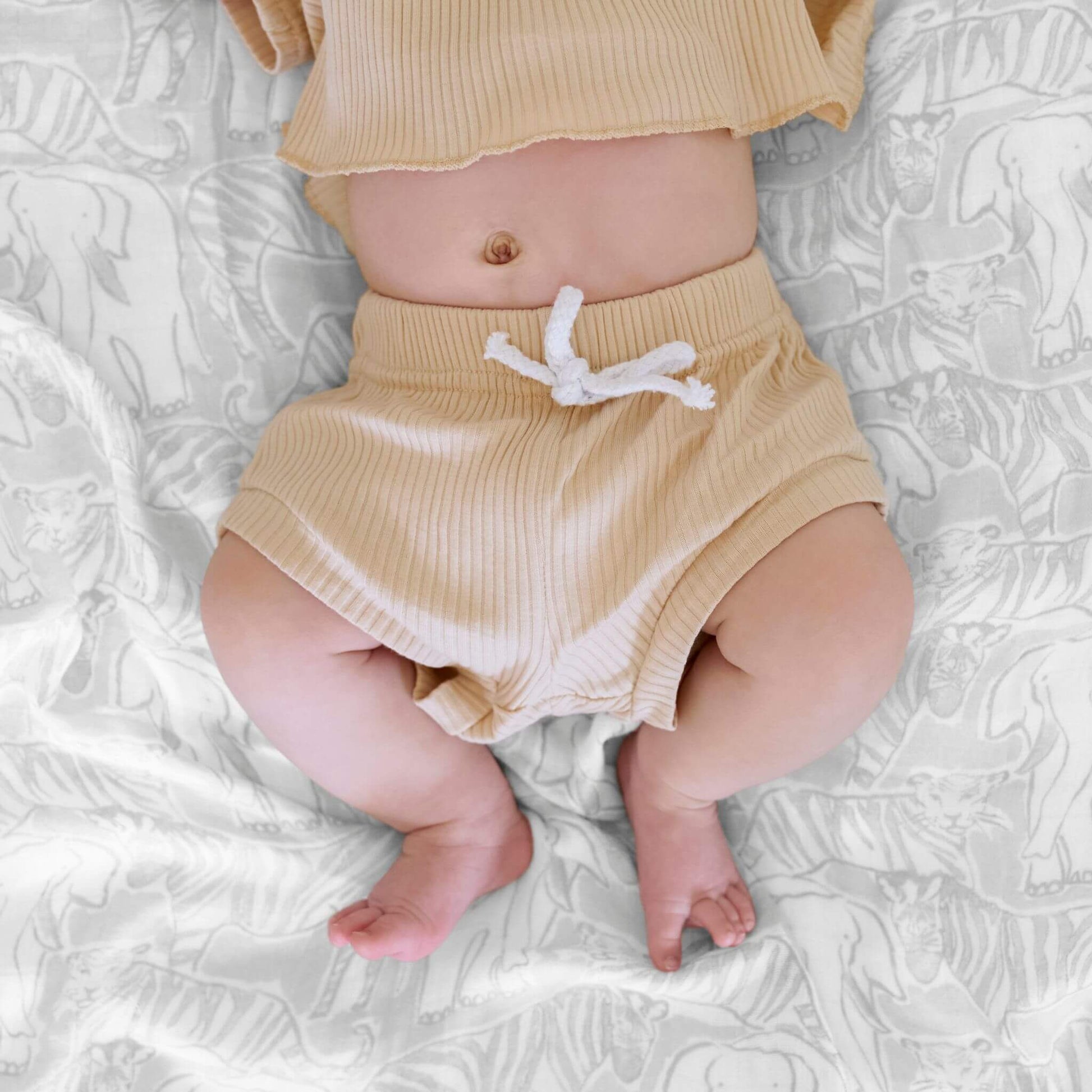 Close-up of a baby lying on an aden + anais Culture Club Silky Soft Swaddle, featuring a grey animal print on breathable bamboo muslin.