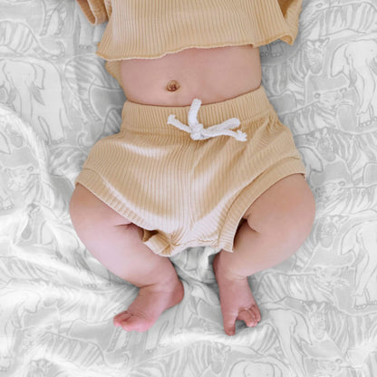 Close-up of a baby lying on an aden + anais Culture Club Silky Soft Swaddle, featuring a grey animal print on breathable bamboo muslin.