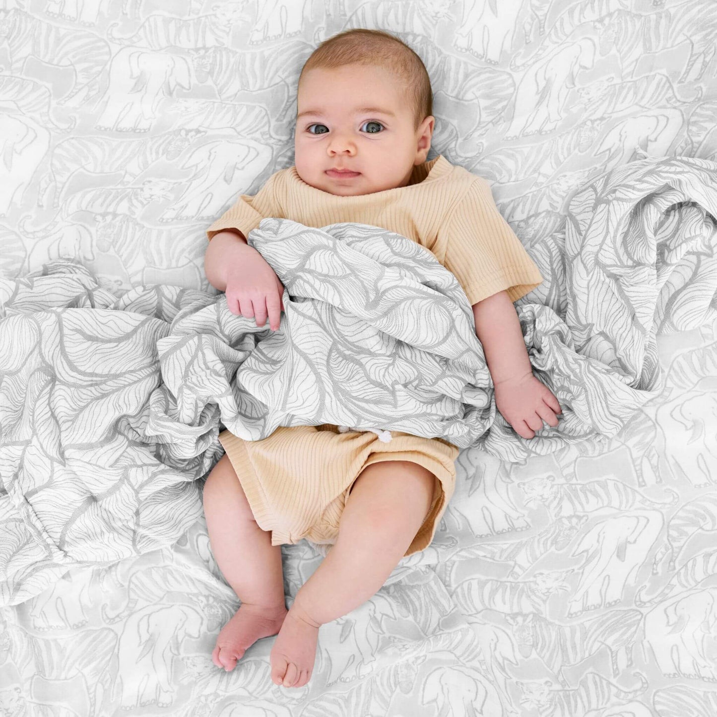 Adorable baby wrapped in an aden + anais Culture Club Silky Soft Swaddle, featuring elegant grey animal and leaf patterns on bamboo muslin.