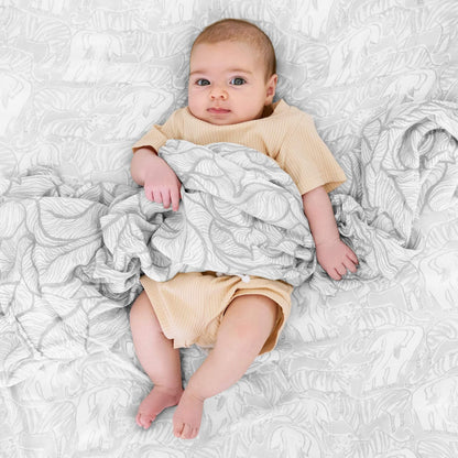 Adorable baby wrapped in an aden + anais Culture Club Silky Soft Swaddle, featuring elegant grey animal and leaf patterns on bamboo muslin.