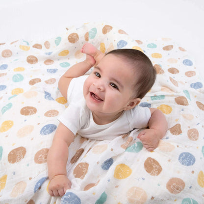 Smiling baby on aden + anais cotton swaddle with Winnie the Pooh silhouette dot pattern in earthy tones and soft muslin texture