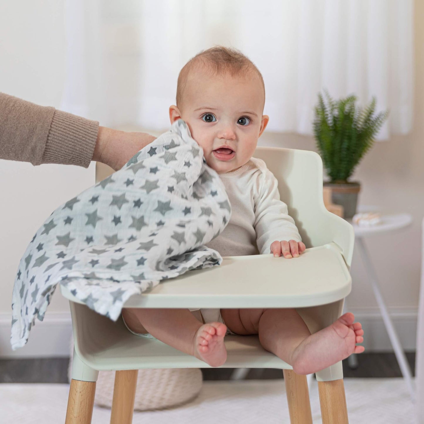 Baby in a highchair being wiped with a star-print muslin square from the aden + anais Twinkle collection.