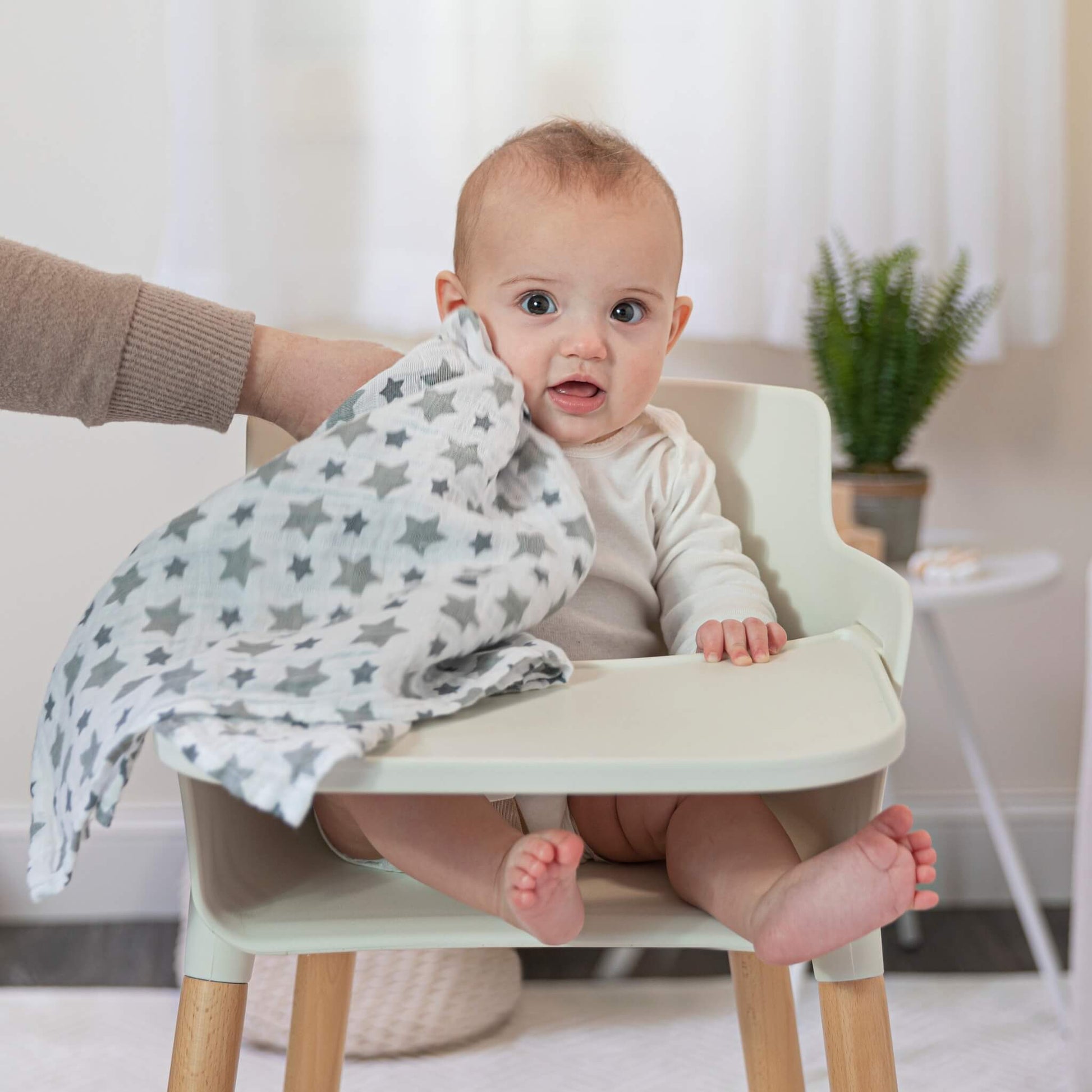 Baby in a highchair being wiped with a star-print muslin square from the aden + anais Twinkle collection.