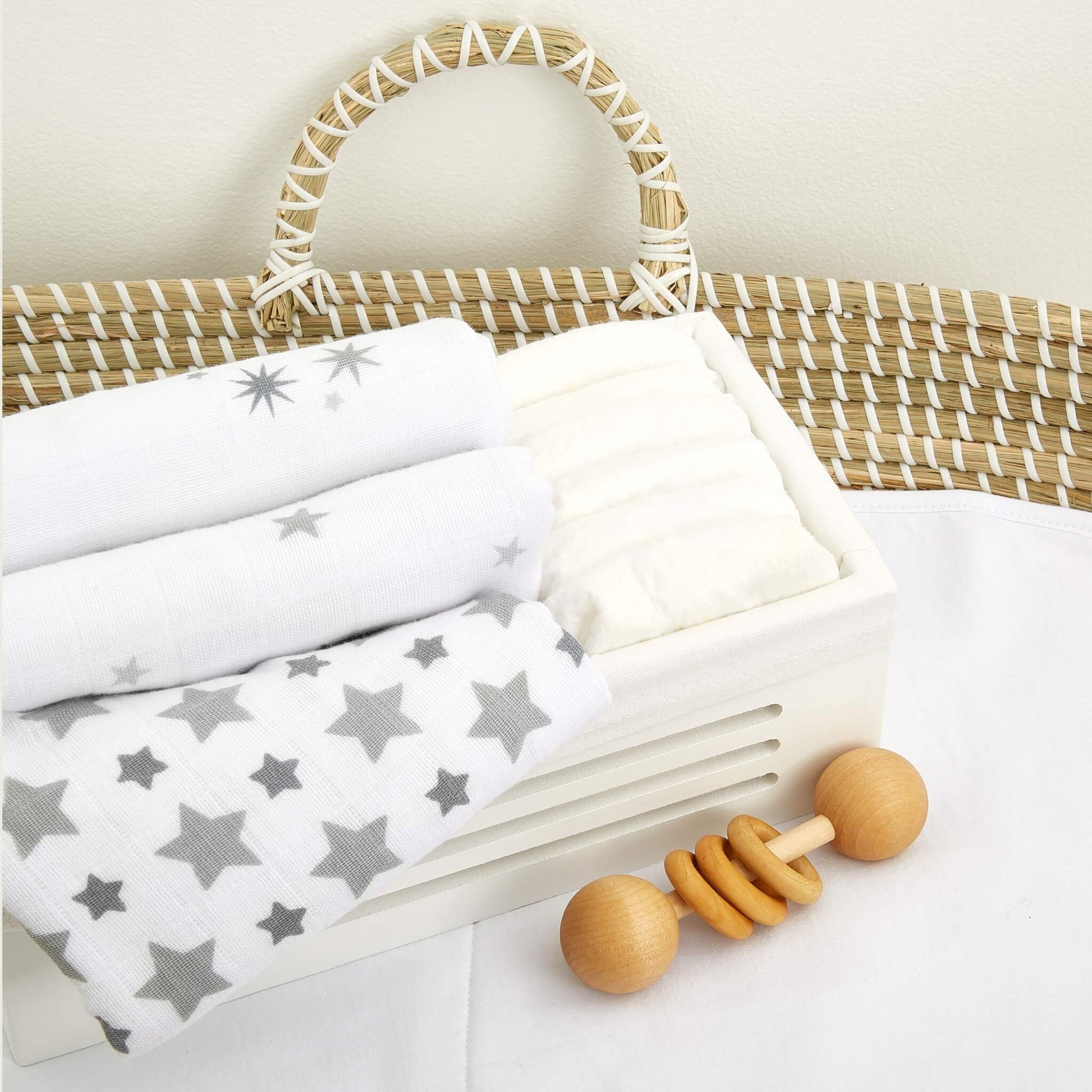 Twinkle muslin squares folded in a nursery basket, styled with white bedding and a wooden rattle.