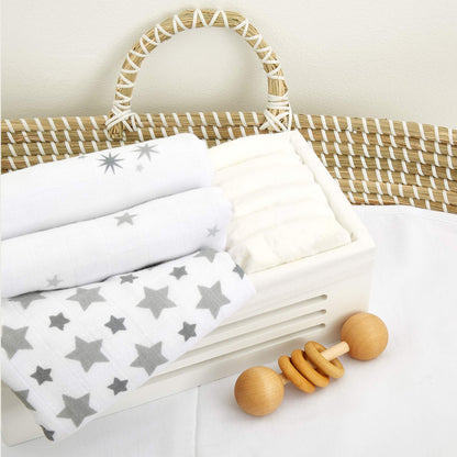 Twinkle muslin squares folded in a nursery basket, styled with white bedding and a wooden rattle.