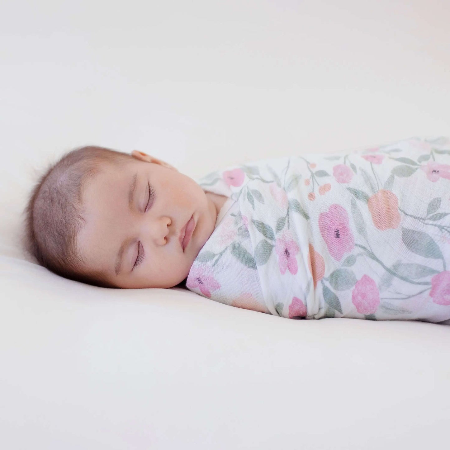 Baby sleeping peacefully wrapped in aden + anais Ma Fleur floral muslin swaddle.