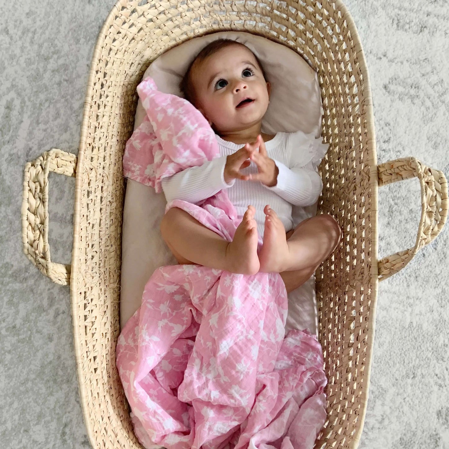 Baby in Moses basket cuddling aden + anais Ma Fleur pink floral cotton swaddle.