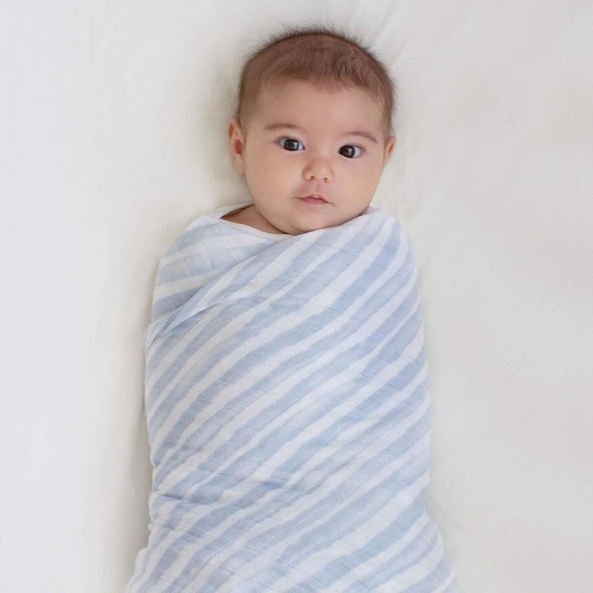 Baby swaddled snugly in aden + anais Rising Star striped cotton muslin blanket. Lightweight, breathable, and perfect for sleep.