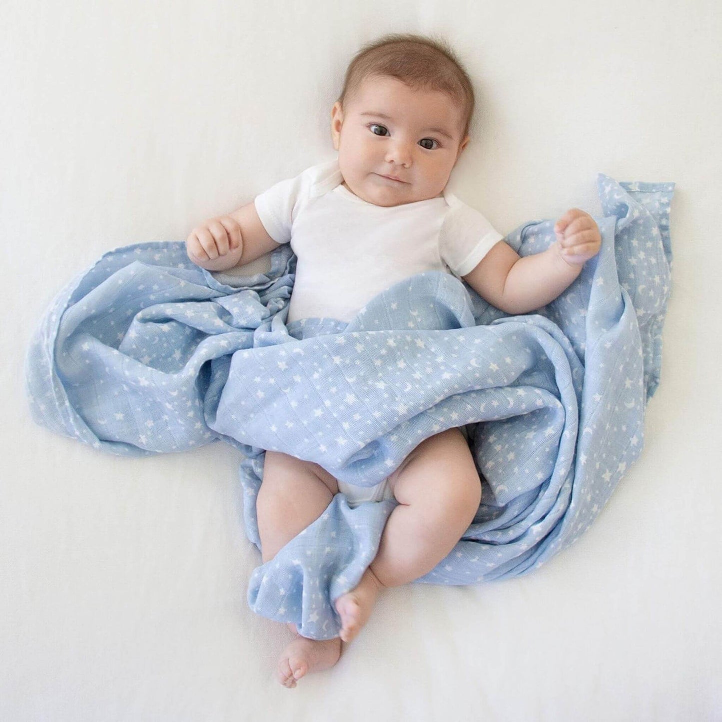 Baby wrapped in aden + anais Rising Star cotton muslin swaddle. The soft blue star print offers breathable comfort for naps or play.
