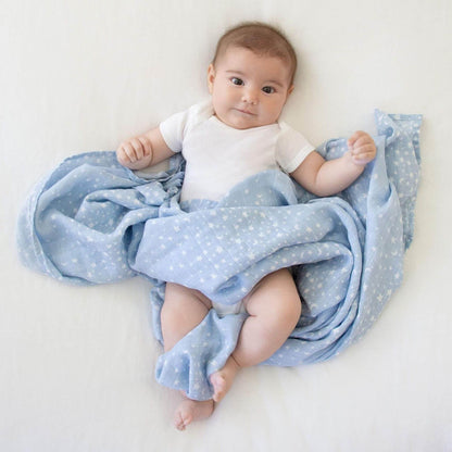 Baby wrapped in aden + anais Rising Star cotton muslin swaddle. The soft blue star print offers breathable comfort for naps or play.