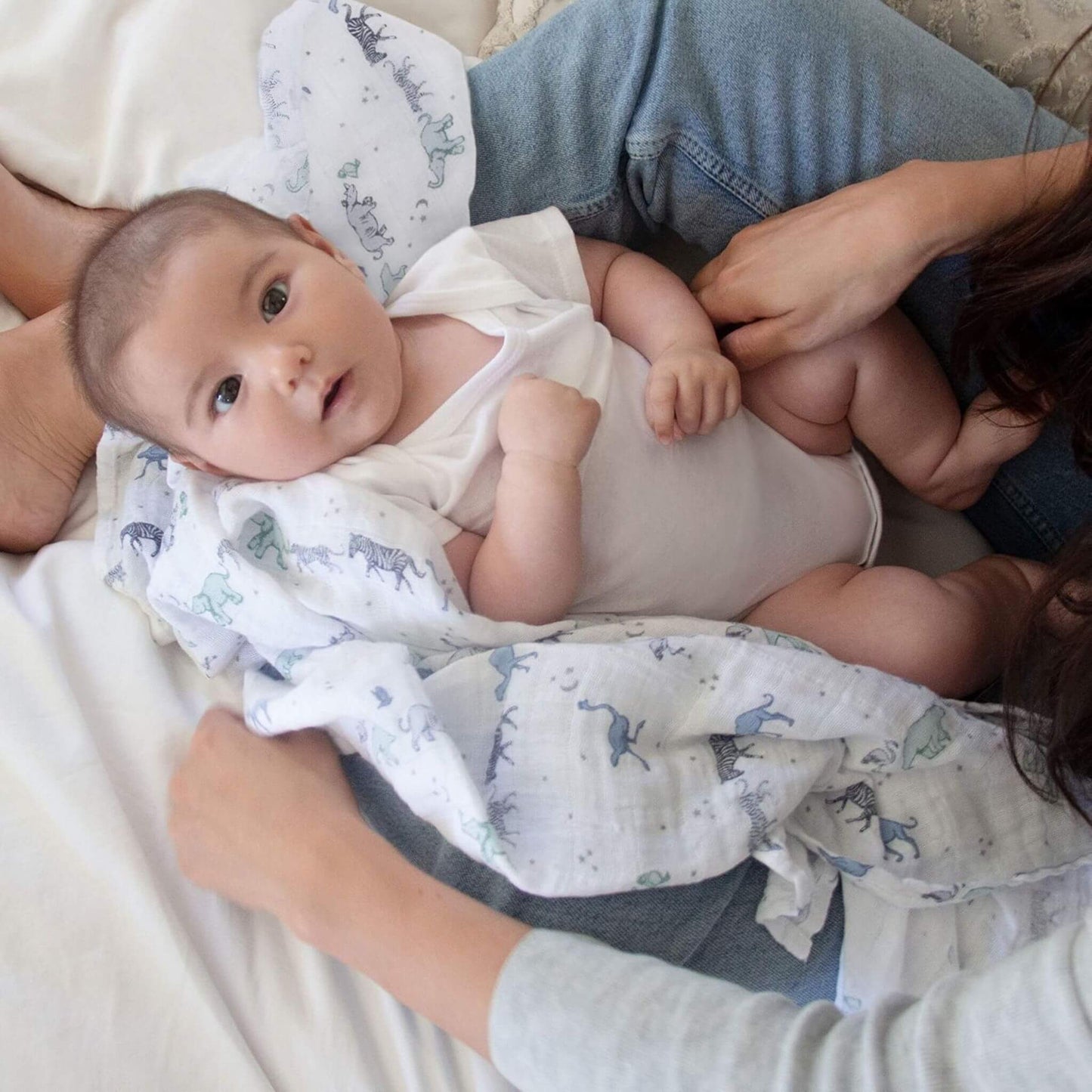 Mother cuddling baby wrapped in aden + anais Rising Star animal print swaddle. Soft muslin fabric is gentle on delicate skin.