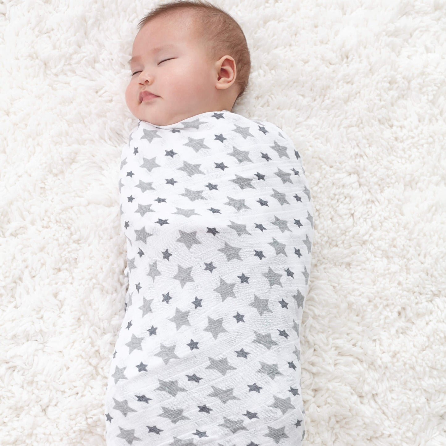 Sleeping baby wrapped in grey star print muslin from aden + anais Twinkle collection. Lightweight and breathable for nap time.