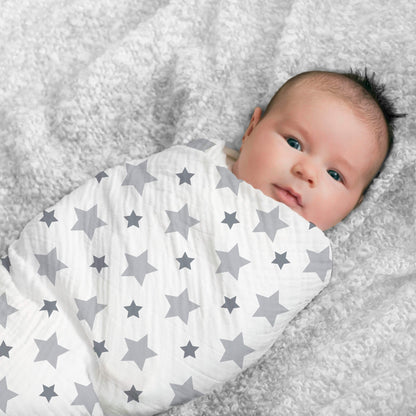 Baby awake and smiling, swaddled in grey star aden + anais cotton muslin. Perfect for soft, breathable newborn comfort.