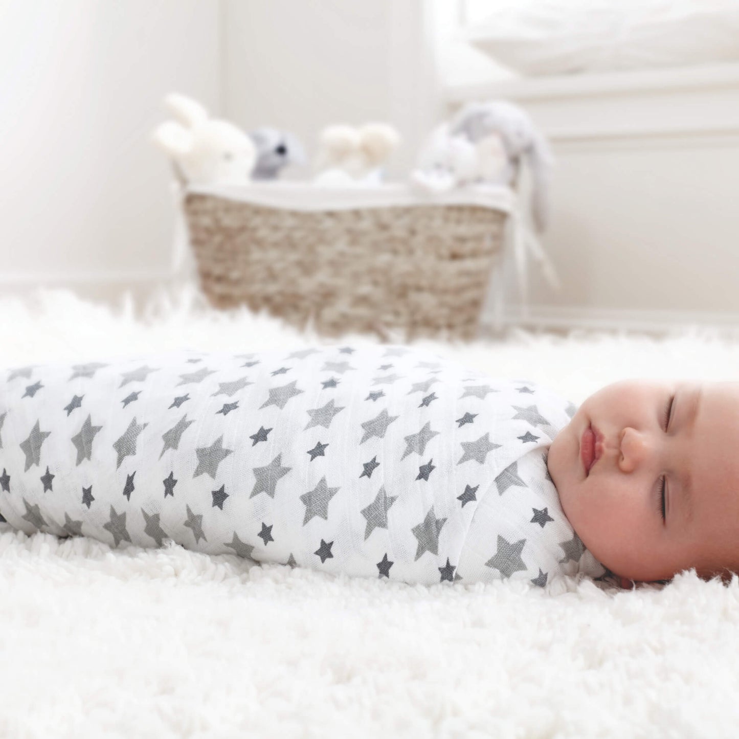 Baby sleeping on soft white rug wrapped in aden + anais Twinkle star swaddle. Gentle muslin fabric keeps baby snug and cosy.