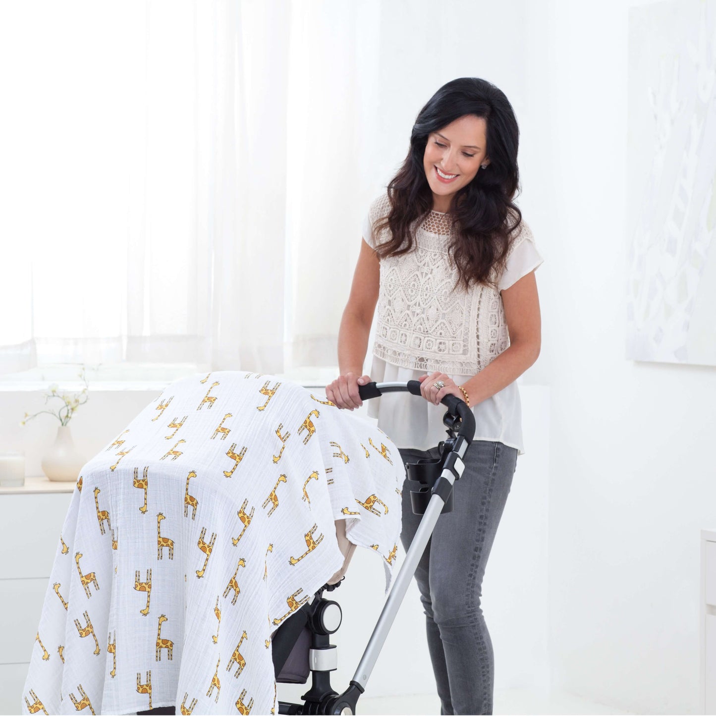 Mother smiling beside pram covered with aden + anais Jungle Jam giraffe swaddle. Breathable fabric, ideal for on-the-go shade.