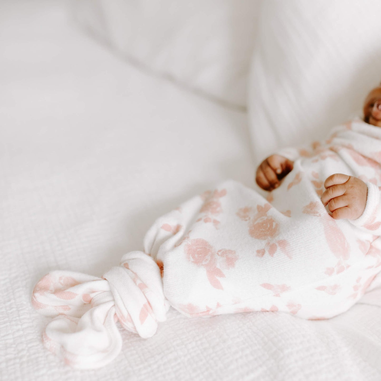 Newborn wearing the aden + anais Rosettes gown and matching knotted hat. Soft floral print in blush pink on cream.