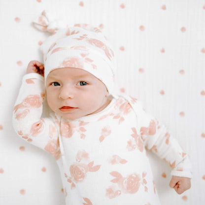 Newborn wearing the aden + anais Snuggle Knit Hat and matching sleep gown in Rosettes print. Soft pink roses on cream background.