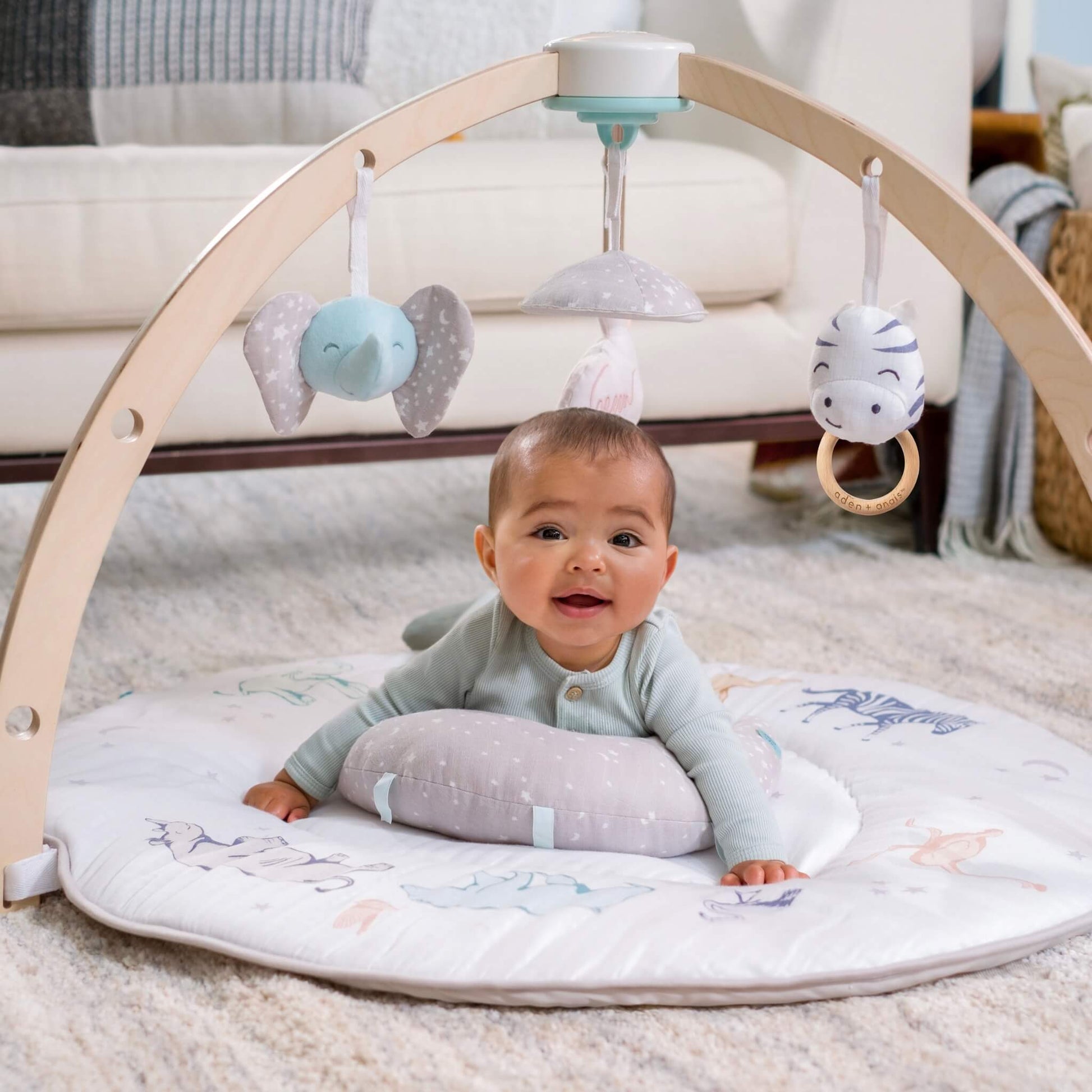 Baby enjoying tummy time on the aden + anais Rising Star Activity Gym. Features eco-friendly muslin mat and soft developmental toys.