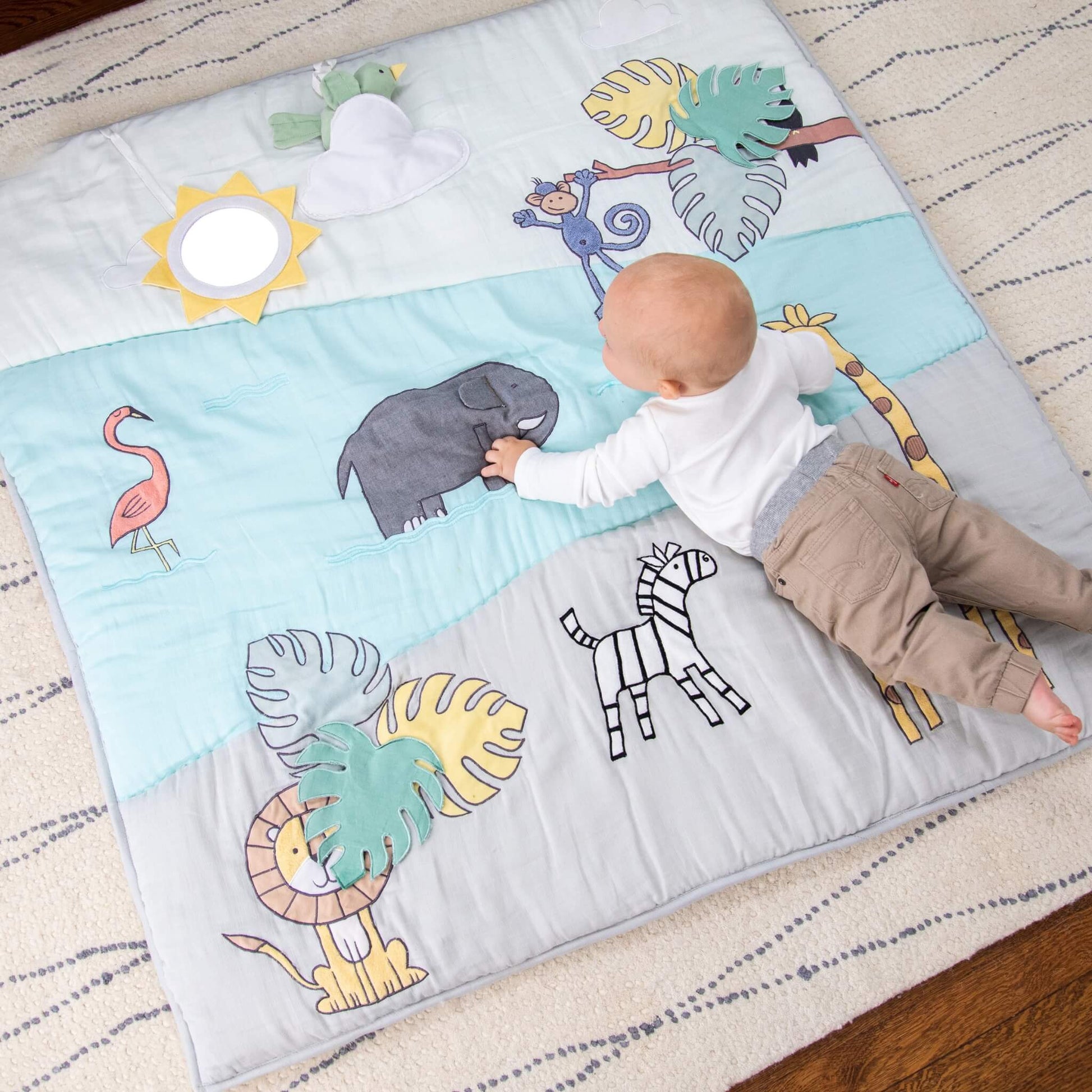 Baby exploring the aden + anais playmat during tummy time. Surrounded by embroidered jungle animals, the mat encourages reaching and discovery.