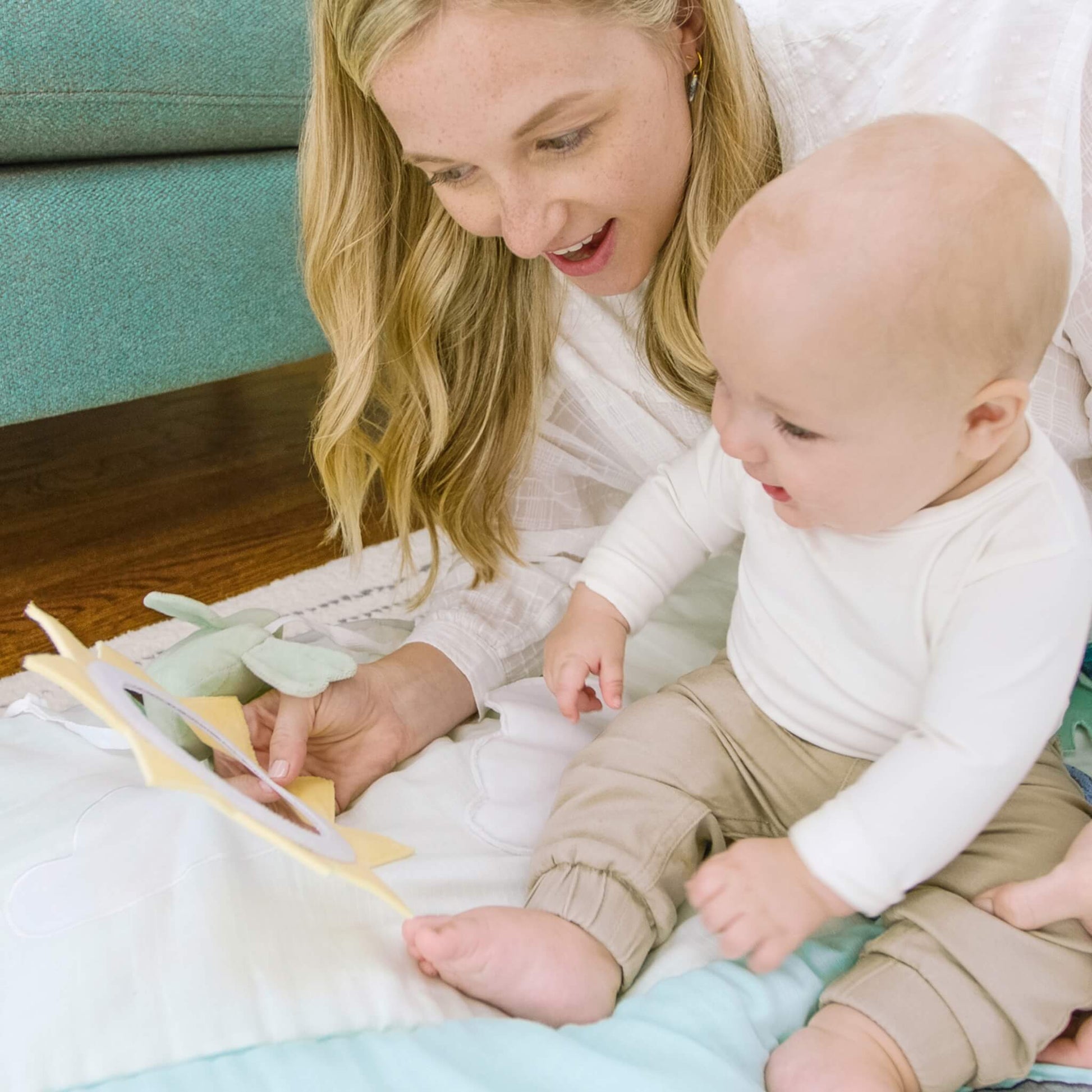 Mother and baby bonding on aden + anais cotton muslin playmat, interacting with the sun mirror and plush bird—ideal for tummy time and sensory play.
