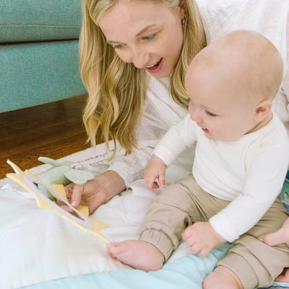 Mother and baby bonding on aden + anais cotton muslin playmat, interacting with the sun mirror and plush bird—ideal for tummy time and sensory play.