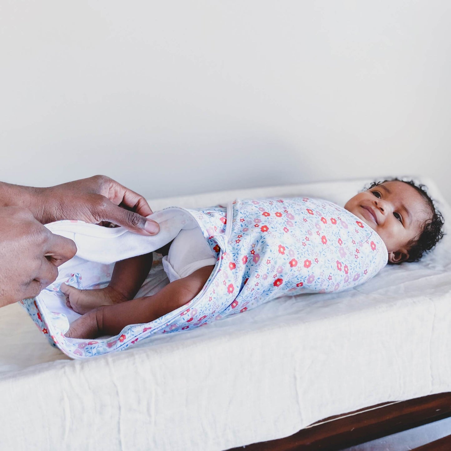 Parent changing baby in aden + anais floral wrap swaddle on a changing mat, with the zip open.
