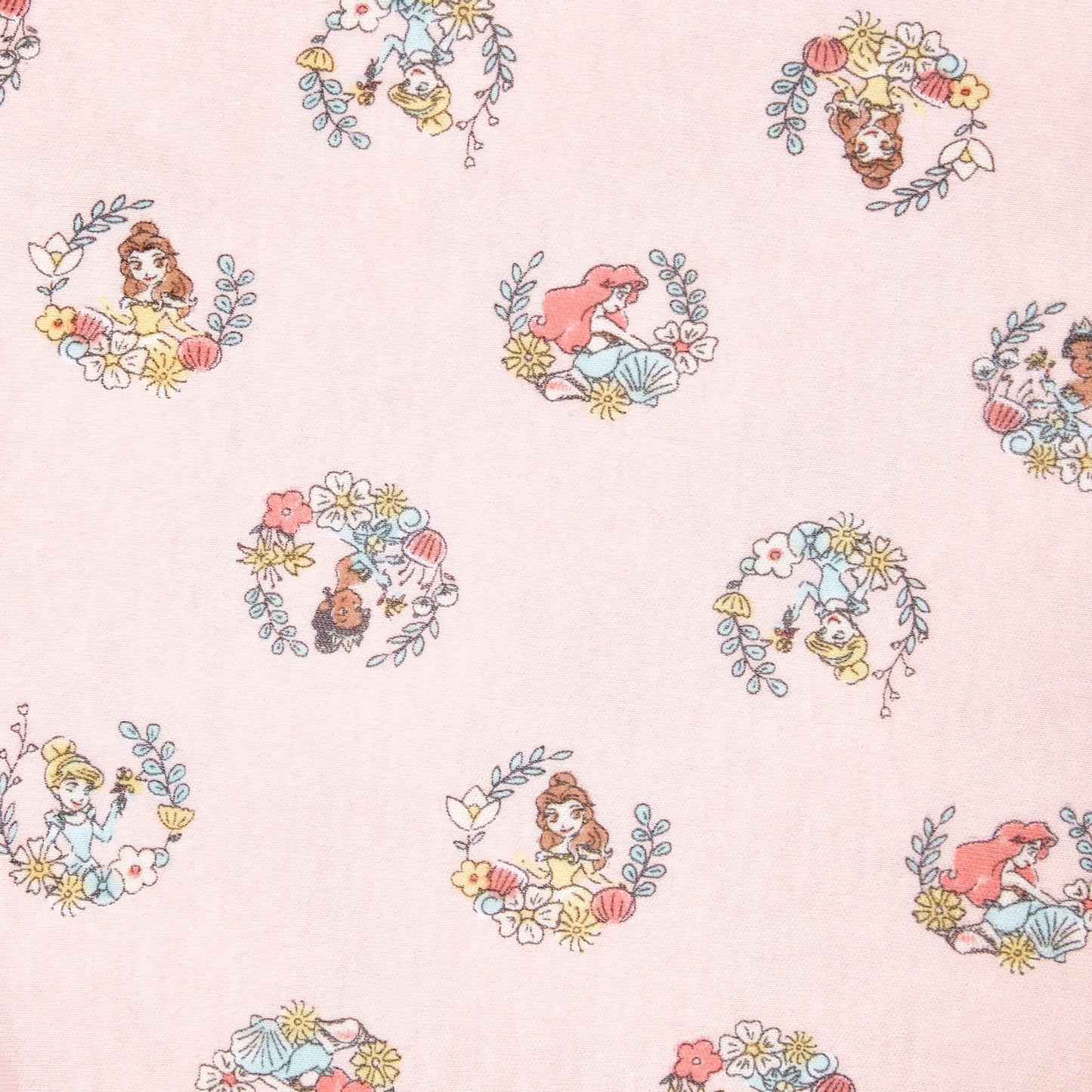 A detailed close-up of the pink swaddle showing repeating circular princess illustrations framed with leaves and flowers, including characters such as Belle, Ariel, and Moana.