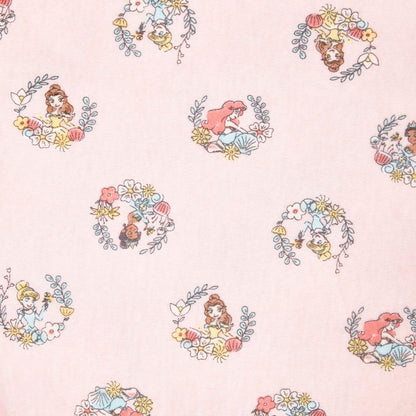 A detailed close-up of the pink swaddle showing repeating circular princess illustrations framed with leaves and flowers, including characters such as Belle, Ariel, and Moana.
