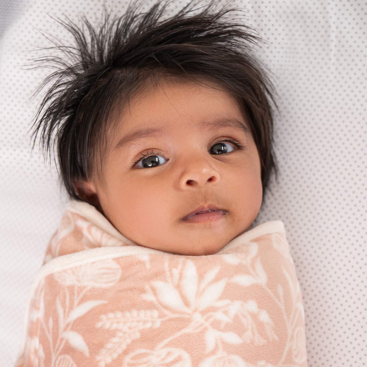 Close-up of newborn swaddled in the aden + anais Garden floral velboa wrap, resting on a soft surface.